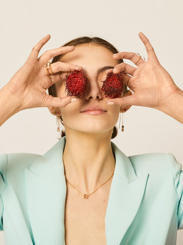 A girl with strange fruit covering her eyes as she models LÚDERE Jewelry